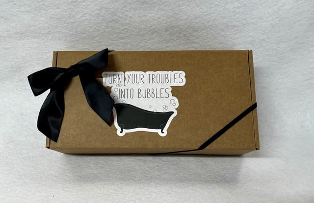 Kraft gift box with a black bow and a “Turn your troubles into bubbles” bathtub sticker