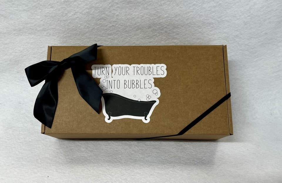Kraft gift box with a black bow and a “Turn your troubles into bubbles” bathtub sticker